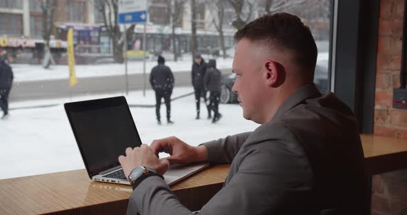 A Man Is Working At A Computer And It Is Snowing Outside The Window