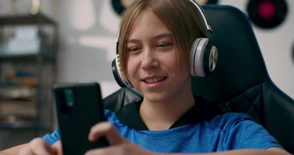 A Teenager Talks on Wireless Headphones While Doing Homework on Phone alt