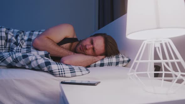 Young Caucasian Man Waking Up and Taking His Smartphone