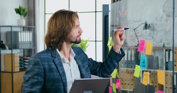 Man Standing Near Glass Wall and Doing Records on it with Black Marker in Modern office