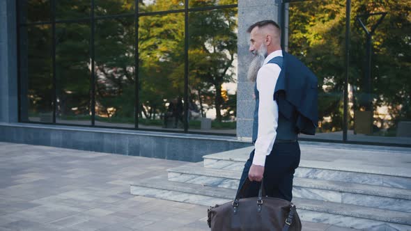 Handsome Bearded Mature Man in Suit Walking Outdoors on Modern Building Background During Sunny Day