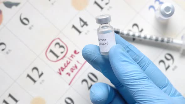 Vaccine Day Concept with Holding Glass Ampoule Vaccine Against Calendar