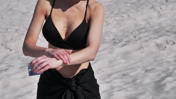 woman in a swimsuit applying lotion to her body on sand background