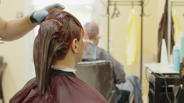 Unrecognizable Person Combs Colored Hair of Young Woman in Salon