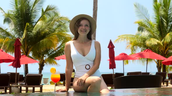 Influencer Girl in Swimwear Sitting in Swimming Pool with Tropical Cocktail