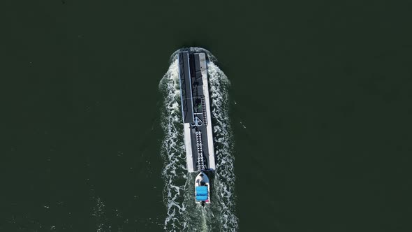 Small boat delivering a large pontoon passes a navigation marker on a river canal. High drone view.