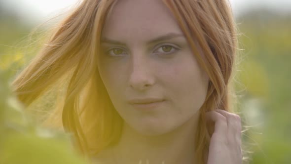 Close-up Portrait of Confident Sensual Girl with Red Hair and Green Eyes Standing on Sunflower Field