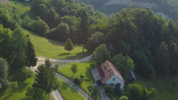 Small countryside farm up in hills between green meadows and forest breeding cows. Aerial 4k view.