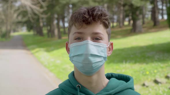 A young man in a medical protective mask looks up and smiles in a country park