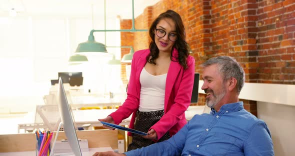 Male and female executives discussing over digital tablet at desk