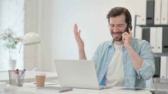 Young Man with Laptop Talking on Smartphone