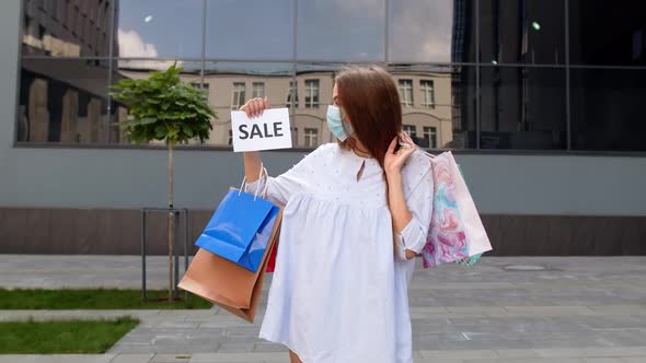 Girl in Protective Mask with Shopping Bags Showing Sale Word Inscription During Coronavirus Pandemic