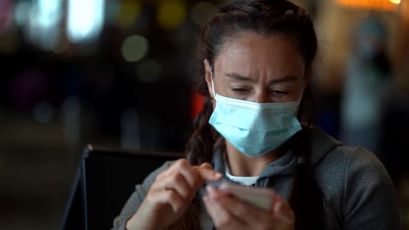 Portrait of a Dark-haired, Pigtailed Middle-aged Woman in a Medical Mask Sitting in a Public Place