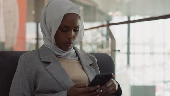 Black Woman in Hijab Surfs Internet on Smartphone in Office