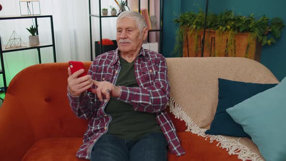 Senior Old Grandparent Works on Mobile Phone Sends Messages Makes Online Purchases at Home Sofa