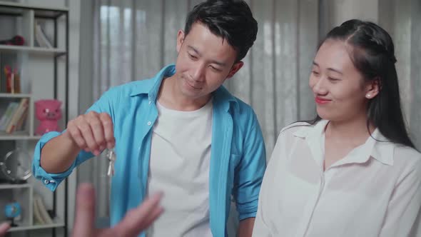 Asian Man Receiving And Looking At The Keys From A Real Estate Agent While Standing With A Woman