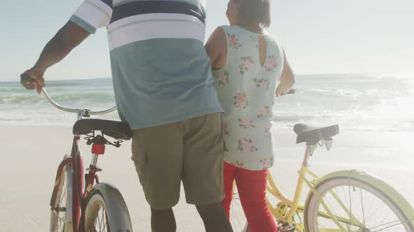 Senior african american couple walking with bicycles on sunny beach