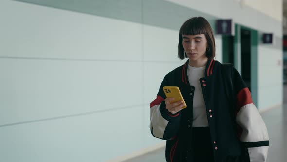 Woman in Bomber Jacket Walking at Airport with Smartphone
