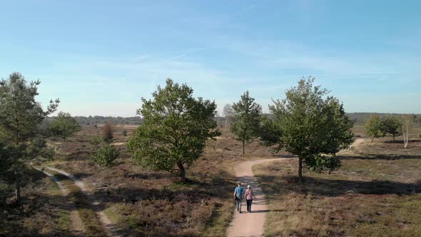 An elderly couple walking along a path through a moorland landscape passing two trees alongside on t