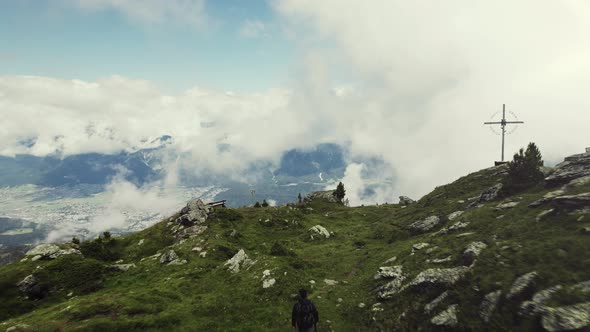 Aerial drone shot of a grass covered mountain top with a person hiking along a small trail. A valley