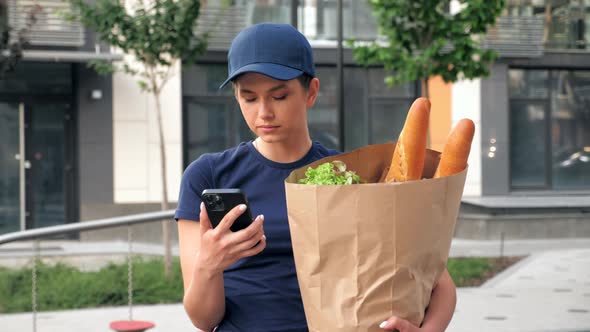 Portrait Food Delivery Woman Courier Uses Smartphone Holds Paper Bag in Hand
