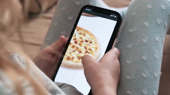 Ordering takeaway food using a smartphone at home, close-up. Little girl chooses pizza on smartphone