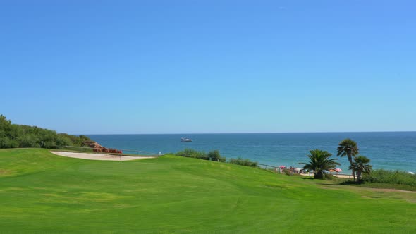 Sight of a Grassy Golf Field a Clear Blue Ocean with a Yacht in the Distance and Some People on the