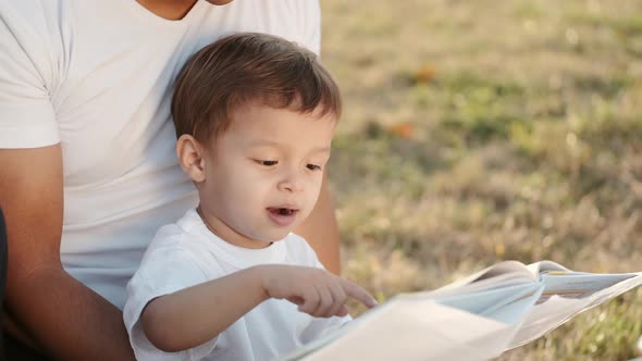 Father and Infant Boy Reading a Book on Blanket