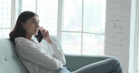 Young Woman Relaxing on Comfortable Couch Enjoying Listening to Lounge Music Live Via Smartphone App