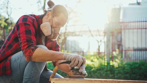 A Young Man in a Construction Respirator Grinds a Parquet Board with a Sander