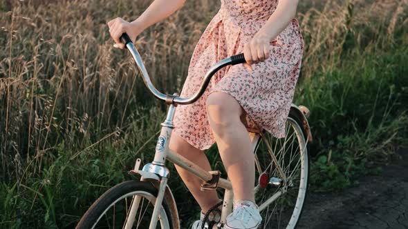 A Girl on a Bicycle is Riding a Field Road at Sunset