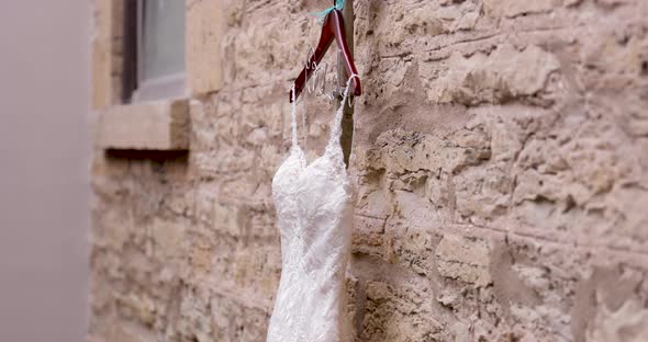 Wedding dress hanging on wooden hanger in front of stone wall inside beautiful church.