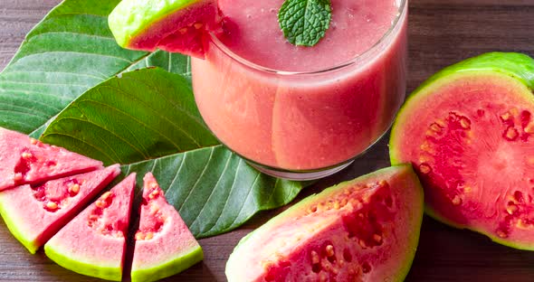 Glass of red guava juice and sliced guava slice on wooden background