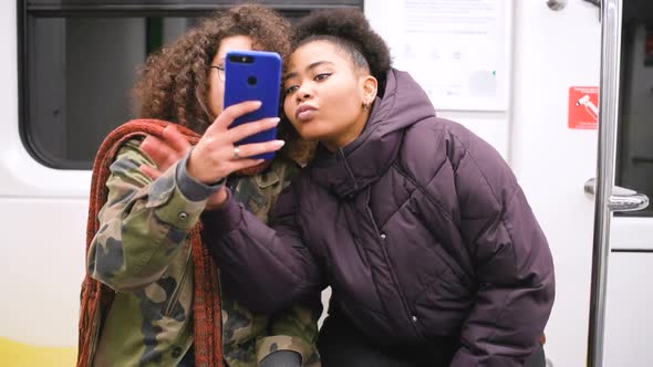 Two young multiethnic women travelling underground using smart phone taking selfie