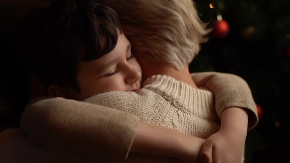 Closeup Back View of Happy Little Child Son Hugging Loving Young Mother Near Christmas Tree