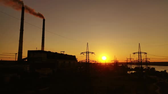 Power station at sunset. Transmission lines near industrial factory with pipes. 