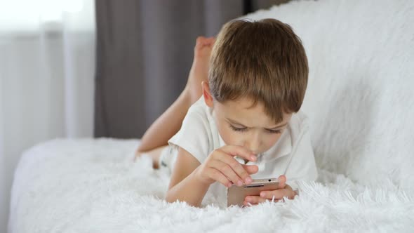 A Cute Boy Uses His Smartphone To Watch a Movie or Play While Lying on the Couch. The Internet