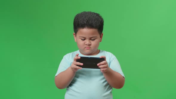 Excited Asian Little Boy Playing Video Game With Mobile Phone In Green Screen Studio