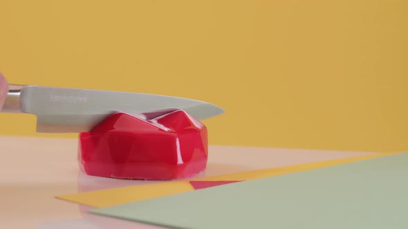 Pastry Chef Cuts Red Cake in the Form of Heart on Colored Yellow Background