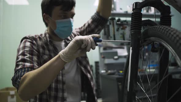 Mechanic Repairing Bicycle in Workshop Wearing Medical Mask Covid 19. Man Repair Bike on Quarantined