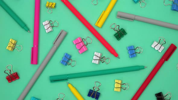 colored ballpoint pens and stationery clips randomly lie on rotating green background. top view. 4k.