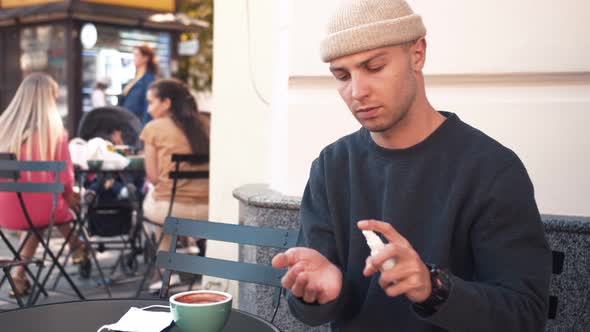 COVID-19 Pandemic Coronavirus. A Young Caucasian Man Using a Hand Sanitizer Spray, at Cafe Outside