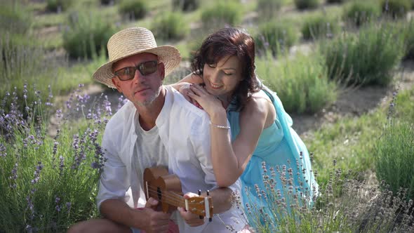 Loving Woman Smiling Holding Shoulder of Talented Man Playing Ukulele in Slow Motion in Sunshine