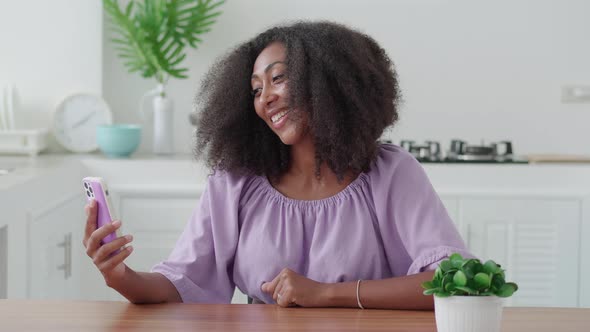 Pleasant Young Multiethnic Woman in Purple Wear Sitting at Wooden Table and Using Smartphone Talking