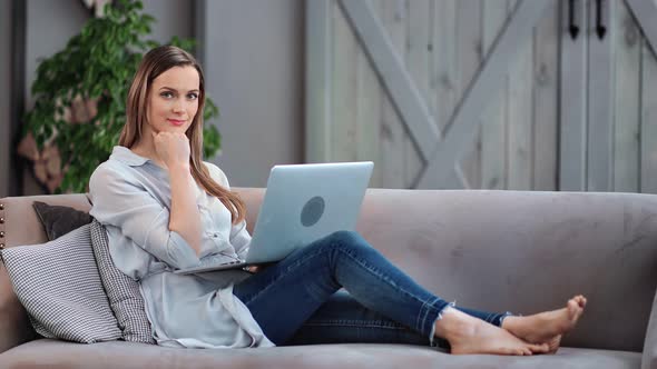 Pleasant Casual Barefoot Girl Sitting on Couch with Laptop Enjoying Break