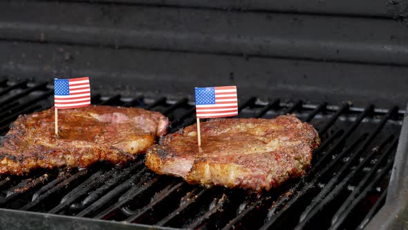 A wonderful shot of two juicy rib-eye steaks sitting on the grill and cooking with two small America
