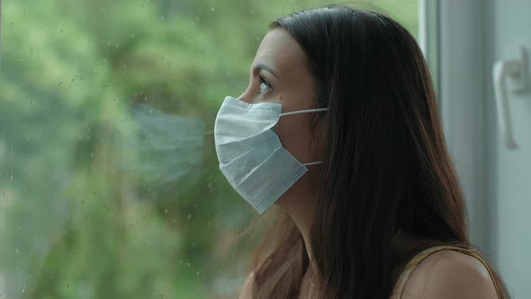 Woman in Face Mask Looks Through the Window