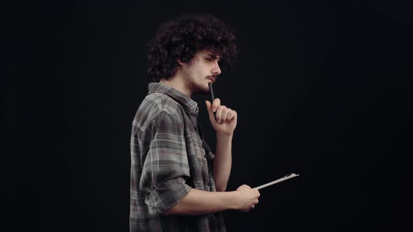 The Attractive Boy with Curly Hair in Profile Thinks Writes Notes with the Pen on the Sheet