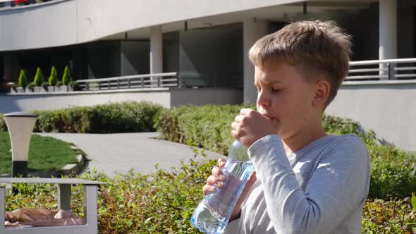 Schoolboy Sitting on Bench and Drinks Clear Still Water From Plastic Bottle