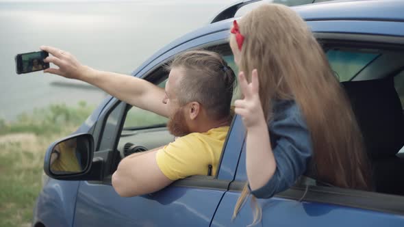 Positive Happy Excited Little Girl and Young Man Taking Selfie Sticking Out Car Window on River Bank